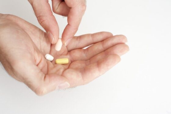Picture of a person taking medication lifting a tablet from a cocktail of three in his hand in a healthcare concept, close up over a white background.