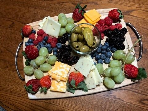 Photo of a charcuterie board filled with delicious, bright colored strawberries, grapes, raspberries, olives, and variety of white and yellow cheeses. 