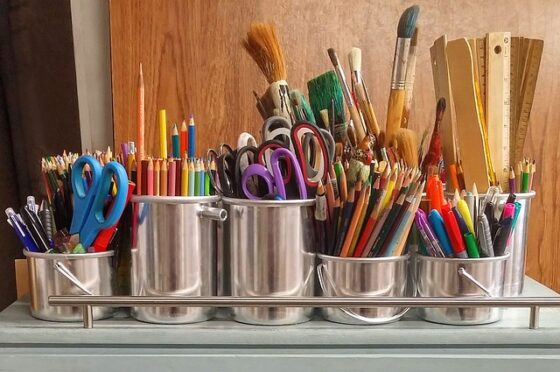 Photo of art supplies in shiny silver pales including scissors, colored pencils, markers, paint brushes, and rulers. 