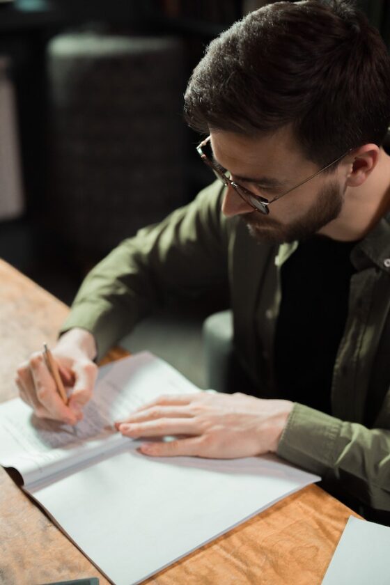 Photo of one male writer's focus on a sheet of paper. He is holding a pencil and wearing a green shirt. 