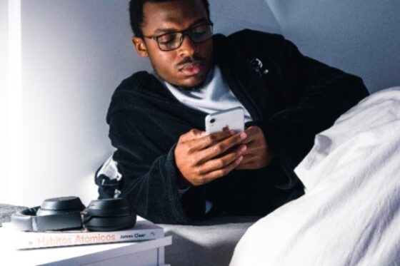 Photo of young man, African American on phone in bed. It is advised to not be on phone so close to trying to sleep.