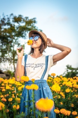 Photo of young woman, Caucasian American out in a field of yellow cheerful flowers on a beautiful spring day with green trees and clear skies.