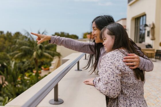 Photo of A Mother Pointing Her Finger while Spending Time with Her Daughter outside looking ahead to the horizon. 
