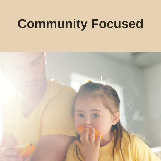 Photo of a father and daughter with down syndrom both wearing yellow t-shirts enjoying an orange. The top of the image displays text "community focused"