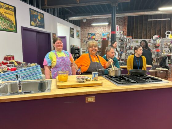 Photo of attendees at Thyme in Your Kitchen. One is stirring the pot, some are watching the instructor and another smiles at the camera. 