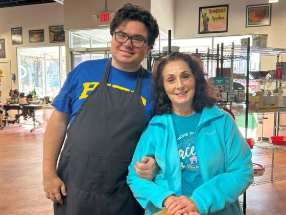 Photo of two attendees at Thyme in Your Kitchen. A tall male Caucasian with dark hair and glasses is wearing a blue t-shirt and black apron. A shorter female Caucasian has long dark hair and is wearing a teal shirt and sweater.   