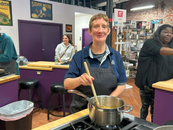 Attendee at Thyme in Your Kitchen smiling and stirring a pot on the stove. 