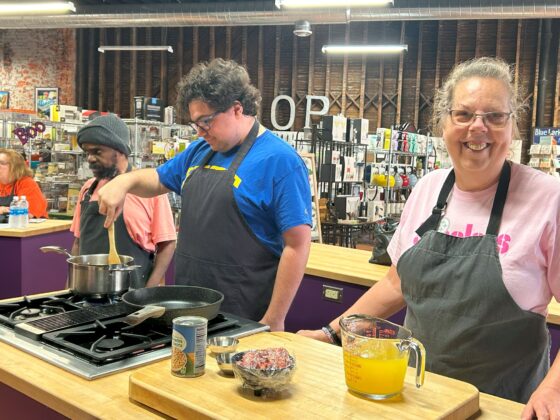 Attendees at Thyme in Your Kitchen smiling and stirring a pot on the stove. 