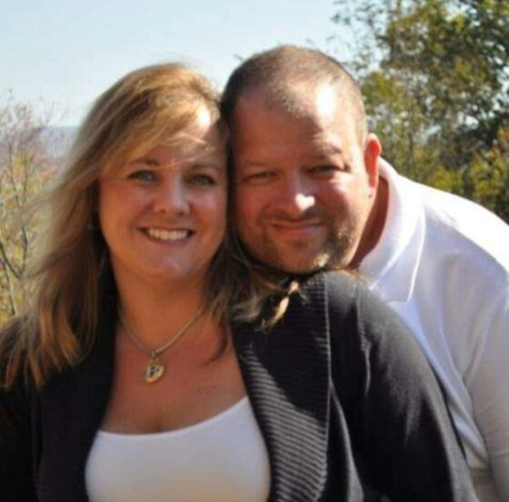 Photo of and provided by owners of Point A to B Transportation LLC, Duane St. Antoine and his wife. They are close and outside on a sunny late summer or early fall day by the look of the trees in the background. He is wearing a white polo and she is wearing a white cami with dark gray seater. They both look happy. 