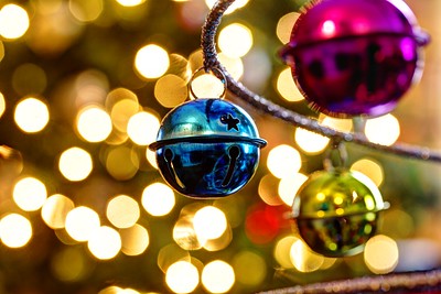Photo of blue, green, and pink jingle bells in front of sparkling bright white lights. Christmas decorations. 