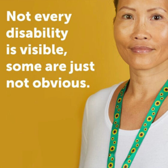 Image of yellow background with a woman wearing a white t-shirt and the Sunflower green lanyard. She has beautiful tan skin and brown eyes. Text in white reads "Not every disability is visible, some are just not obvious." 