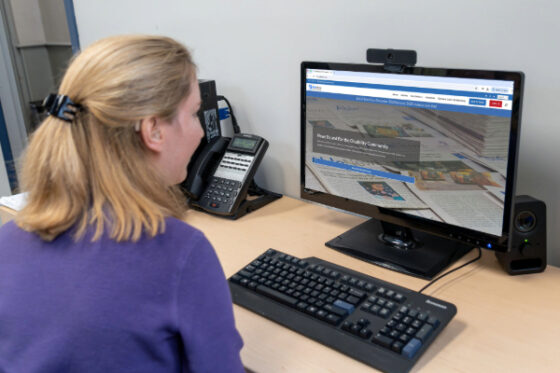 Photo of a young, blonde, woman wearing a purple sweater and looking at a computer screen which displays the Able News at The Viscardi Center website. 