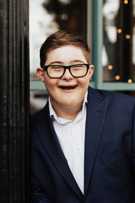 Photo of Max with a big smile wearing dark glasses and a suit. 