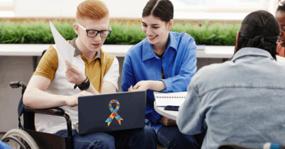 Photo of college students looking at a laptop computer. The back of the computer has a puzzle piece Autism awareness ribbon.